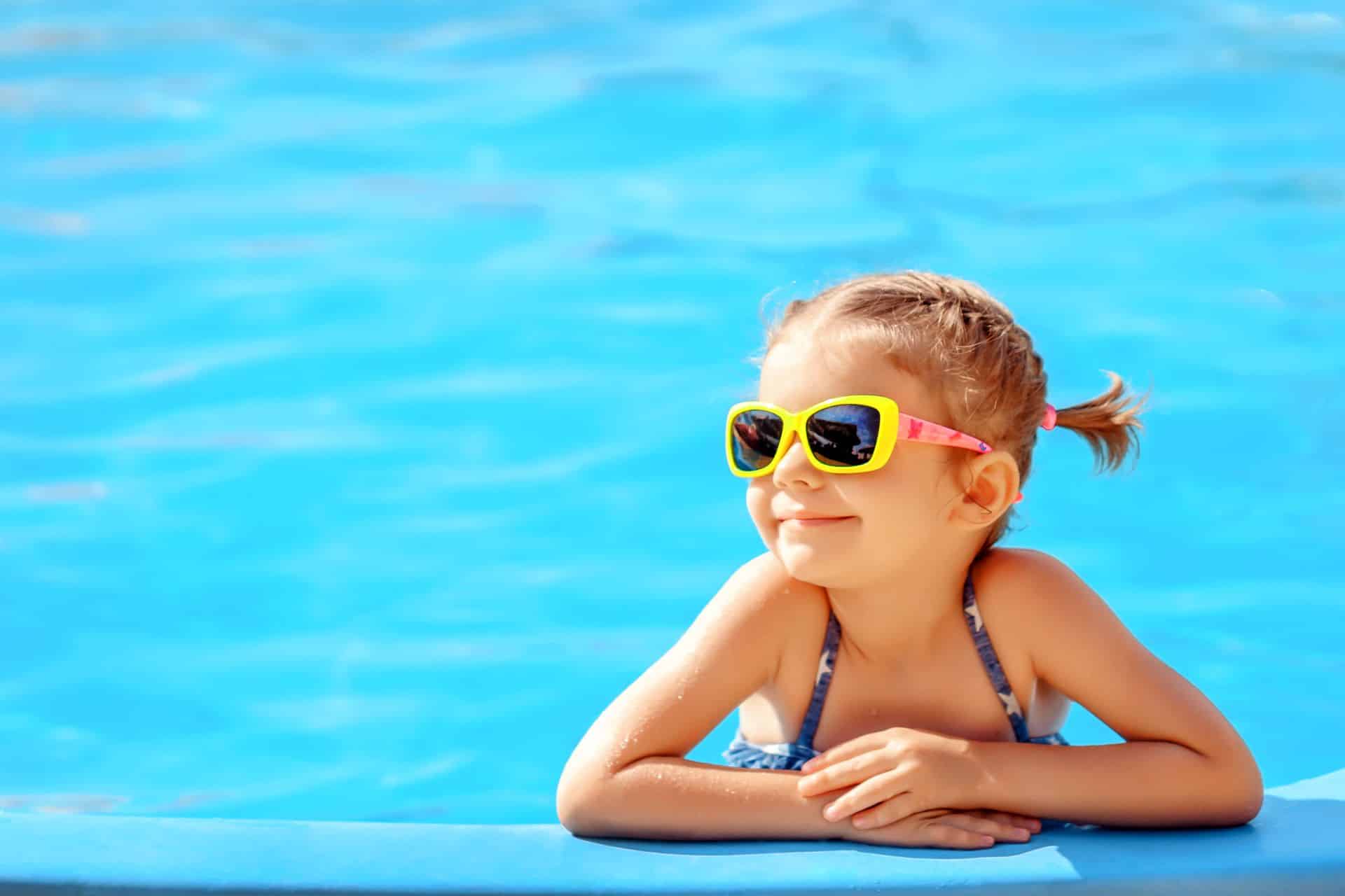 Lächelndes niedliches kleines Mädchen mit Sonnenbrille im Pool an einem sonnigen Tag.