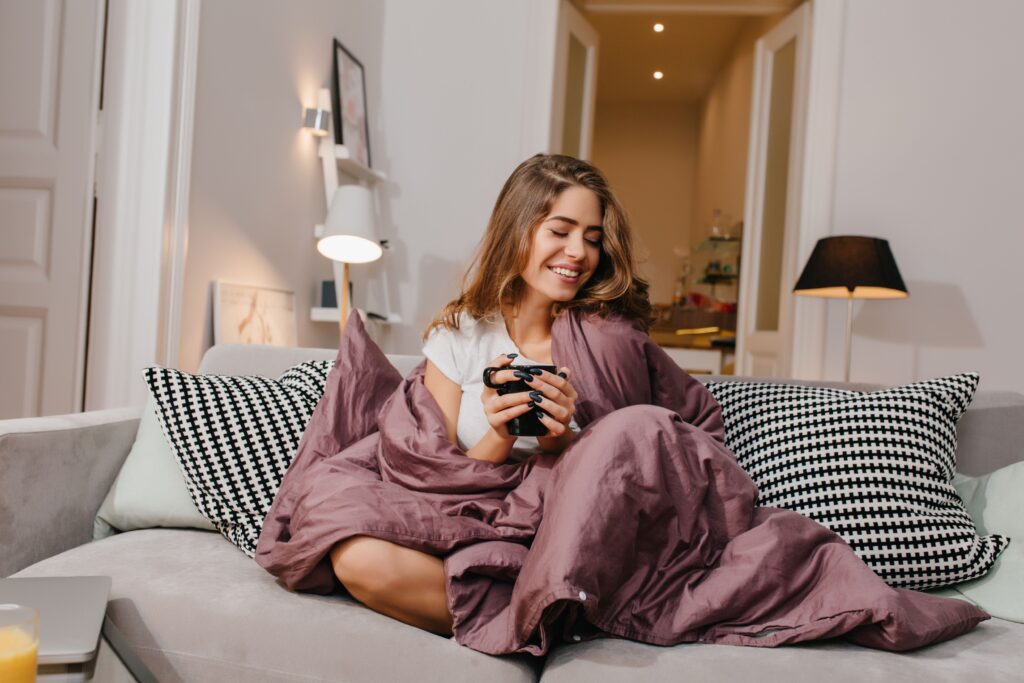 Eine Frau sitzt auf der Couch in einer Decke eingehüllt