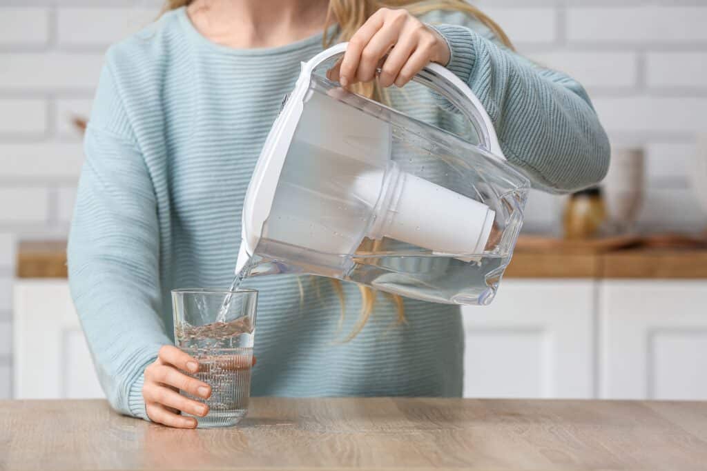 Eine Frau gießt sich Wasser aus einem Wasserfilter ein