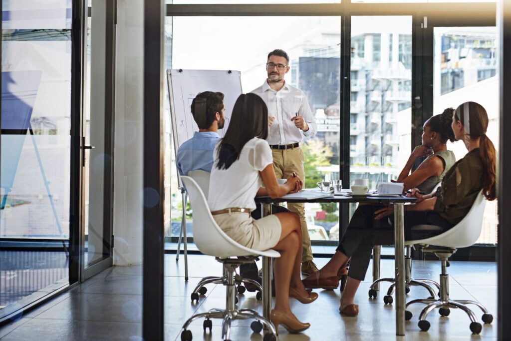 Eine Gruppe von Mitarbeitern bei einem Teammeeting in einem Konferenzraum, während ein Trainer Konzepte zur Einführung eines ERP-Systems erklärt.