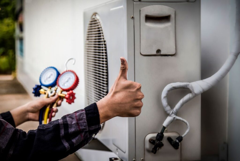 echnician giving thumbs up while holding vacuum sensor gauges near an HVAC unit