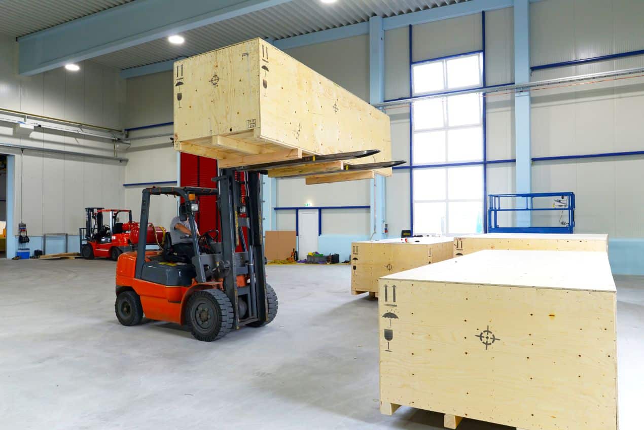 Gabelstaplerfahrer hebt große Holzkiste in moderner Lagerhalle