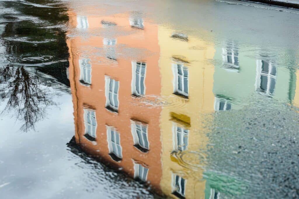 Mehrgeschossige Wohnhaeuser spiegeln sich nach einem Regenschauer in einer Pfuetze auf dem Asphalt
