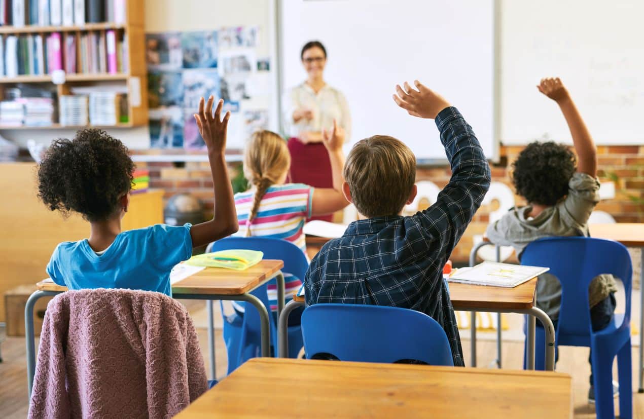 Schueler im Klassenzimmer heben die Haende beim Unterricht – motivierte Lernumgebung in einer internationalen Privatschule Berlin