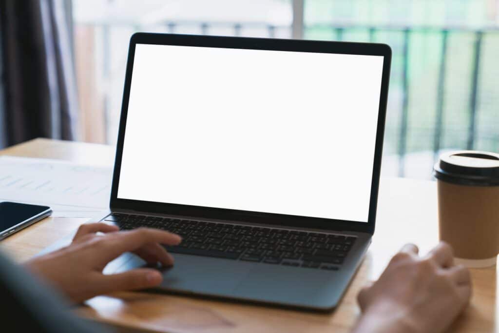 Person nutzt ein Macbook mit leerem Bildschirm und Kaffeebecher auf dem Tisch, Darstellung des digitalen Neuanfangs nach dem Macbook verkaufen