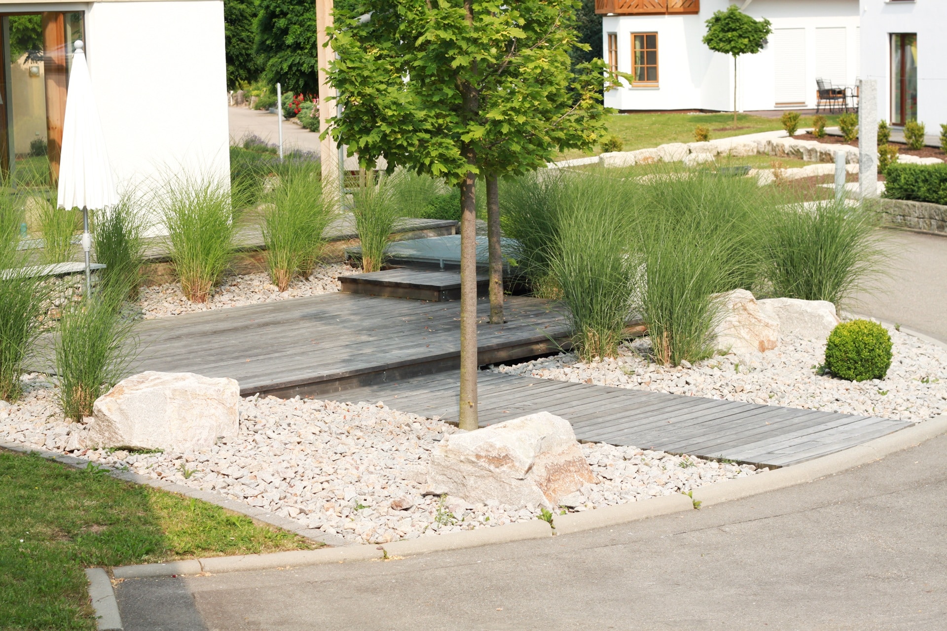 Moderner Garten mit Holzsteg, Ziergräsern und Steinen | Travertin